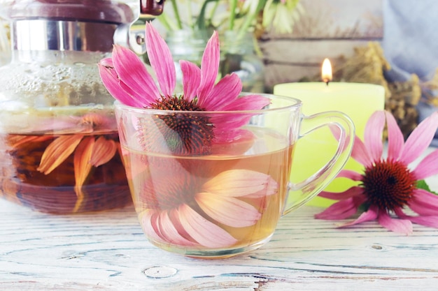 Heiltee aus frischen Echinacea-Blüten und Minze, in einer Glastasse und Teekanne, auf einem Holztisch