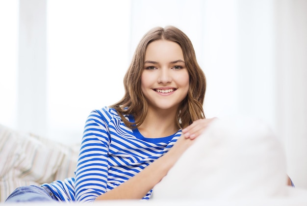 Heim- und Glückskonzept - lächelndes Teenager-Mädchen, das zu Hause auf dem Sofa sitzt