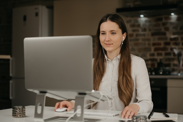 Heimarbeit. Eine kaukasische Frau mit Kopfhörern, die fern an ihrem Laptop arbeiten. Eine Geschäftsfrau in einem weißen Hemd, die Geschäft an ihrem Hauptarbeitsplatz macht.