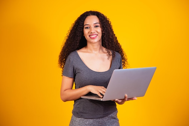 Heimarbeit! Porträt der aufgeregten jungen Afrofrau, die Laptop-Computer lokalisiert über gelbem Hintergrund hält. Exemplar für Text.