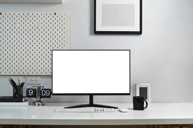 Heimbüro-Arbeitsplatz mit leerem Computerbildschirm, Kaffeetasse und Schreibwaren gegen die weiße Wand