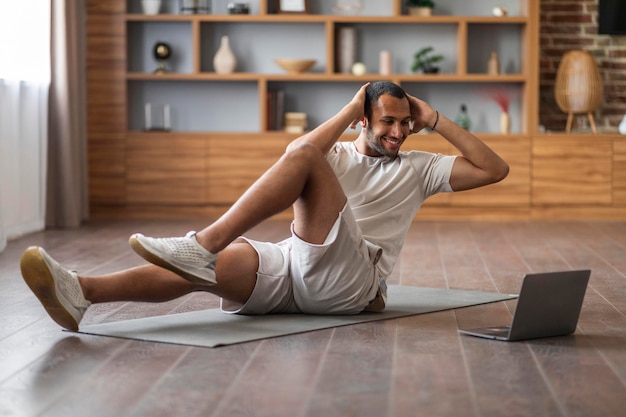 Heimtraining Sportlicher Schwarzer trainiert mit Laptop im Wohnzimmer