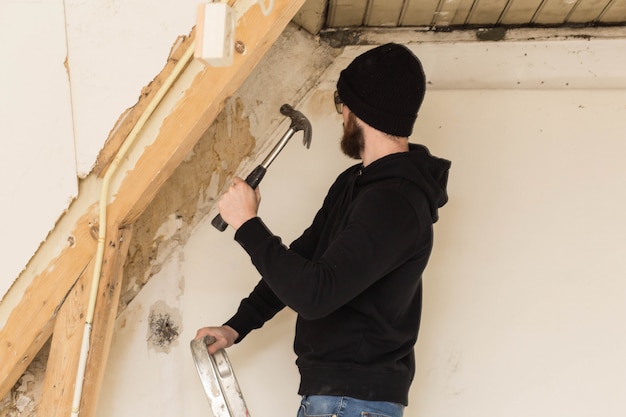 Heimwerker, der auf einer Leiter steht und ein Haus, unter Verwendung der Werkzeuge wie ein Hammer erneuert