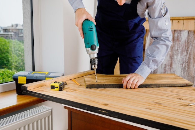 Heimwerker in blauer Uniform arbeitet mit automatischem Schraubendreher der Elektrizität. Konzept der Hausrenovierung.