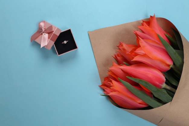 Heiratsantrag. Strauß Tulpen, goldener Ring mit Diamant in Geschenkbox auf Blau on