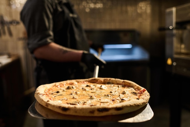 Heiße, appetitliche traditionelle italienische Pizza auf einem Metalltablett, das vom Küchenchef gehalten wird