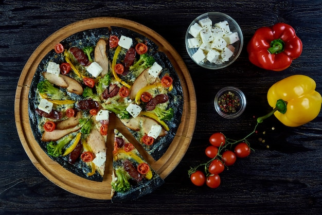 Heiße aromatisierte köstliche italienische Pizza auf schwarzem Teig mit Fleisch, Gemüse, Käse und Gewürzen