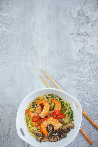 Heiße asiatische Wok-Nudeln mit Garnelen und Pilzen, Ramen, grauer Hintergrund, Kopierraum