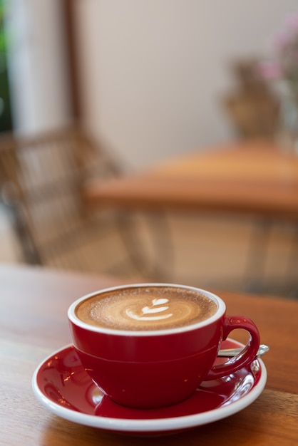 Heiße Kaffeetasse mit Lattekunst in der roten Schale auf hölzerner Tabelle im Caférestaurant