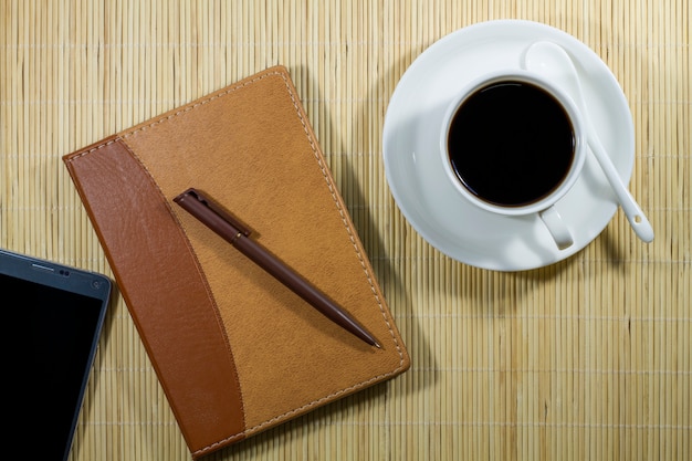 Foto heiße kaffeetasse mit notizbuch und mobile auf dem schreibtischgeschäftsmann