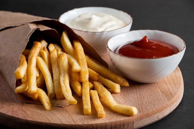 Heiße knusprige Pommes in einer Papiertüte auf schwarzem Hintergrund Leckeres amerikanisches Fast Food