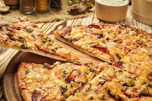 Heiße, köstliche hausgemachte Pizzascheibe mit schmelzendem Käse auf einem rustikalen Holztisch, der zum Essen bereit ist