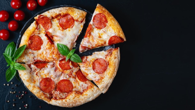 Heiße Peperoni-Pizza und Kochzutaten Tomaten-Basilikum auf schwarzem Betonhintergrund