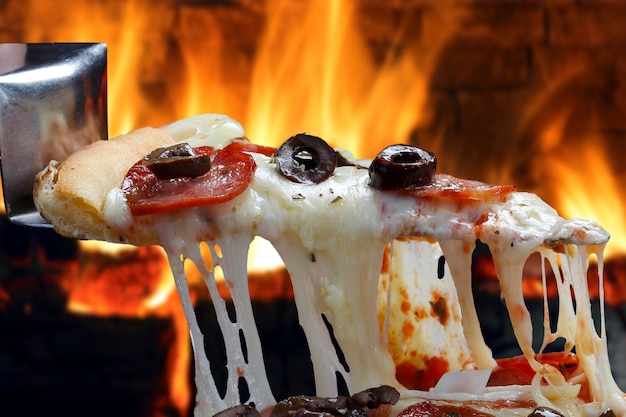 Heiße Pizzascheibe mit schmelzendem Käse mit Holzofen im Hintergrund.