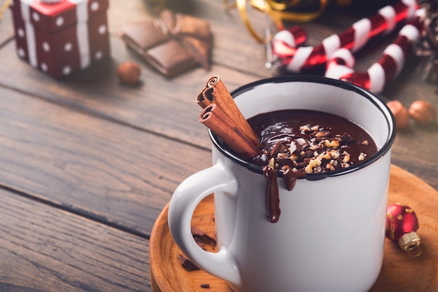 Heiße Schokolade Hausgemachte würzige heiße Schokolade mit Zimt-Haselnuss-Zerkleinerung in Emaille-Becher auf altem Holzhintergrund Getöntes Bild Gemütliche saisonale Feiertage