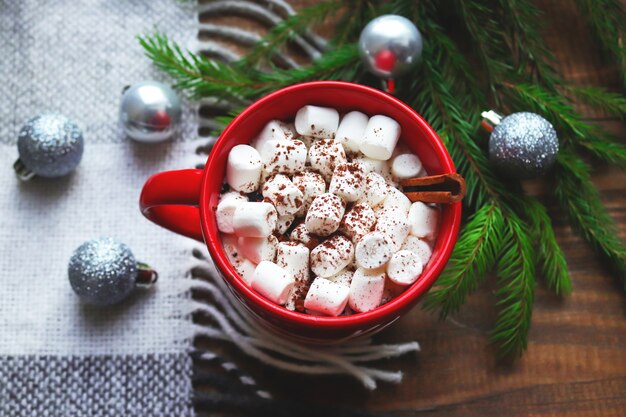 Heiße Schokolade in einem roten Becher mit Marshmallows auf einem Holz mit Plaid- und Tannenzweigen