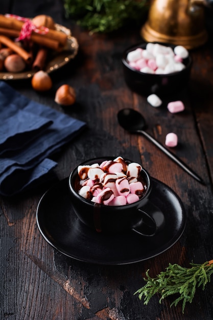 Heiße Schokolade mit Marshmallow-Bonbons in schwarzer Keramikschale auf alter dunkler Holzoberfläche. Selektiver Fokus.