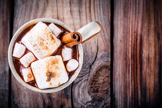 Heiße Schokolade mit Marshmallows und Zimt im Becher auf Holzhintergrund