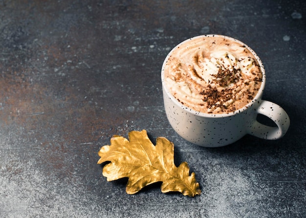 Heiße Schokolade oder Tasse Kaffee mit Schaum und mit goldenem Blatt auf dunklem Hintergrund