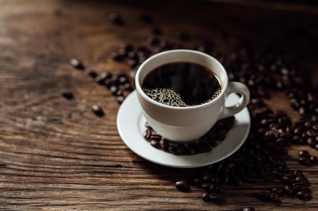 Heiße schwarze Kaffeetasse und Kaffeebohnen auf Holztisch mit Tageslicht am Morgen