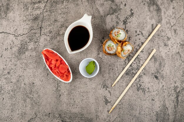 Heiße Sushi-Rollen, Sojasauce und Wasabi auf Steinoberfläche.