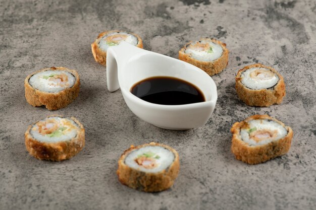 Heiße Sushi-Rollen und Sojasauce auf Steintisch.