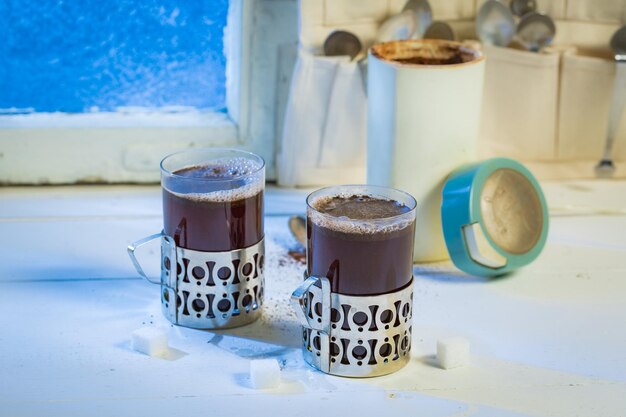 Heiße Tasse und Kaffeekanne mit Löffeln durch gefrorenes Fenster