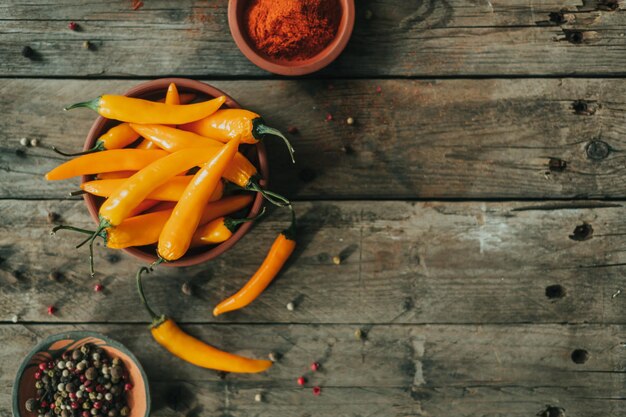 Heiße thailändische gelbe Chilischoten in einer keramischen braunen Steingutschüssel auf einem alten hölzernen Hintergrund. Bunte Paprika (sortiert) mit Erbsen und Paprika