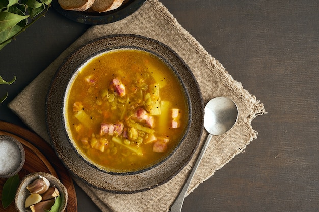 Heiße Wintersuppe mit gehackten grünen Erbsen, Schweinefleisch, Speck, geräuchert auf dunkelbraunem Holztisch