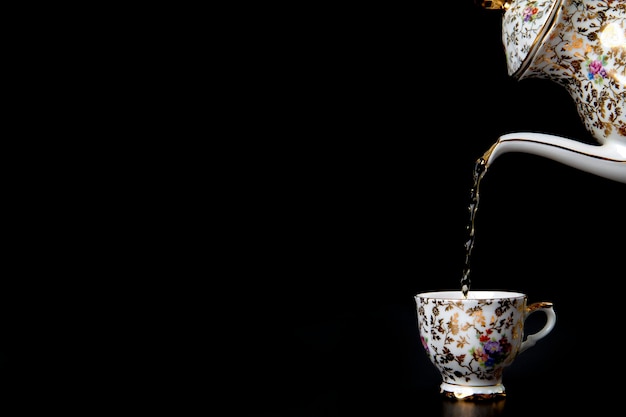 Heißen Tee in Vintage-Tasse auf schwarzem Hintergrund gießen, flüssige Bewegung in einer Tasse, antikes Geschirr mit co