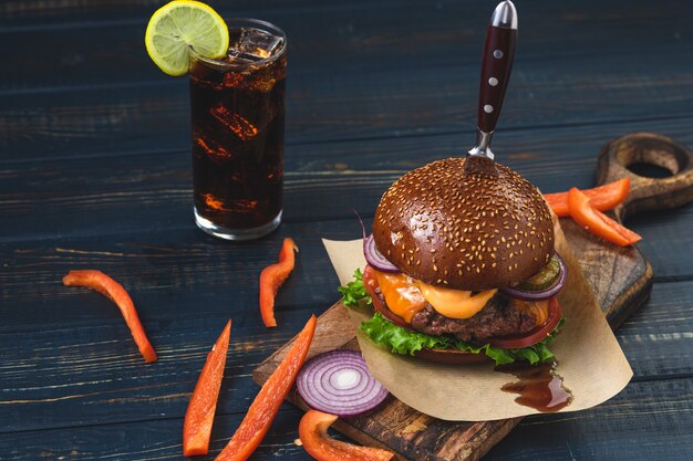 Heißer Burger mit einem Glas Eisgetränk auf einem hölzernen Hintergrund. Rustikaler Stil.