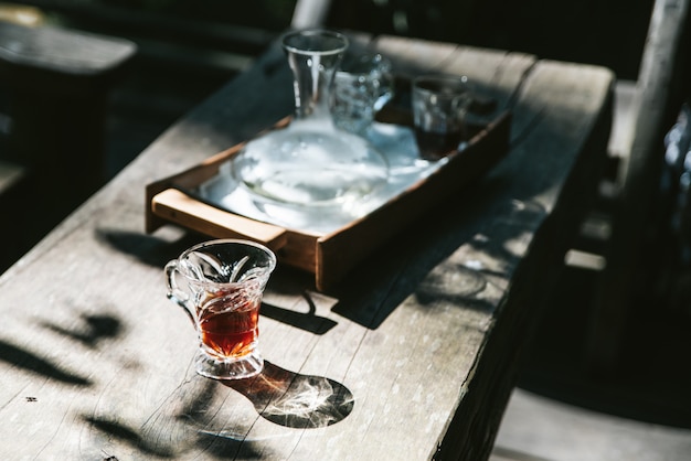 Heißer filterkaffee im trinkglas auf holztisch mit hartem sonnenlicht.