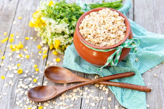 Heißer Haferbrei in einem Tontopf auf einem Holztisch mit einem Blumenstrauß.