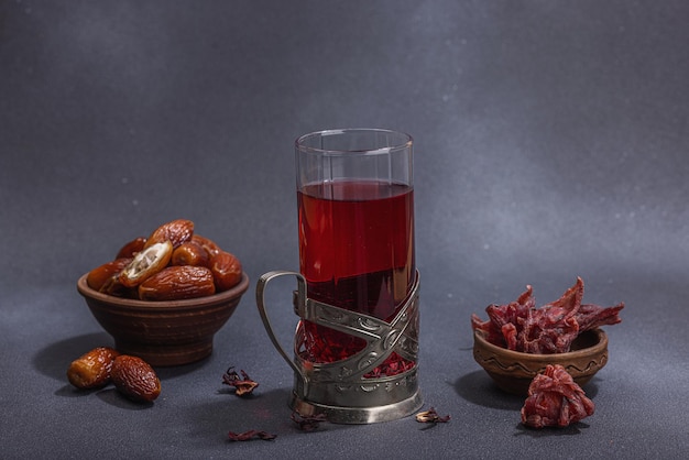 Foto heißer hibiskustee mit datteln, traditioneller ramadan-kareem-konzeptsnack für iftar- oder suhoor-mahlzeit auf dunklem steinbetonhintergrund, ein arabischer süßer leckerbissen, hartes licht, dunkler schatten aus nächster nähe