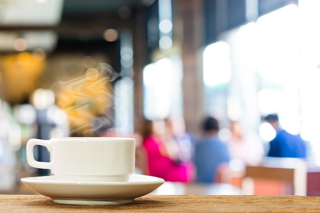 heißer kaffee auf holztisch mit unschärfeleuten im caféhintergrund