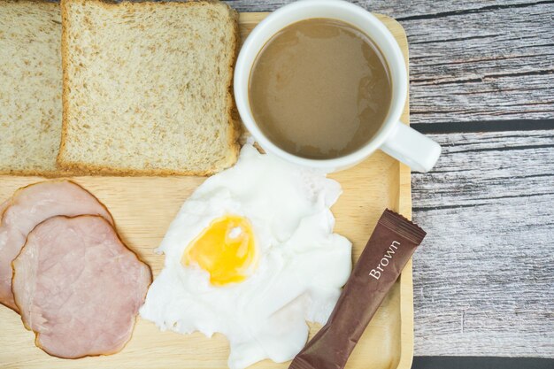 Heißer Kaffee, Ei, Schinken und Brot auf Holztisch zum Frühstück