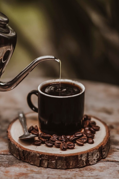 Heißer Kaffee im schwarzen Becher mit Kaffeebohnen auf der Holzplatte