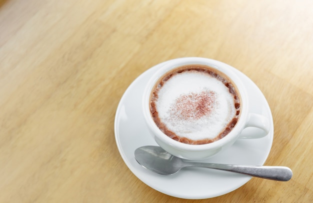 Heißer Kaffee in der weißen Schale mit Metalllöffel auf Holztischhintergrund