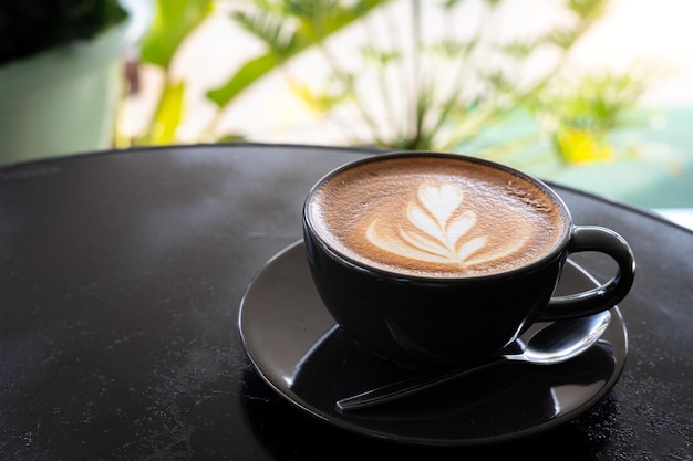 Heißer Kaffee Latte mit Latte-Art-Milchschaum im Becher auf schwarzem Holzschreibtisch in der Draufsicht Als Frühstück in einem Café im Cafeduring-Geschäftsarbeitskonzept