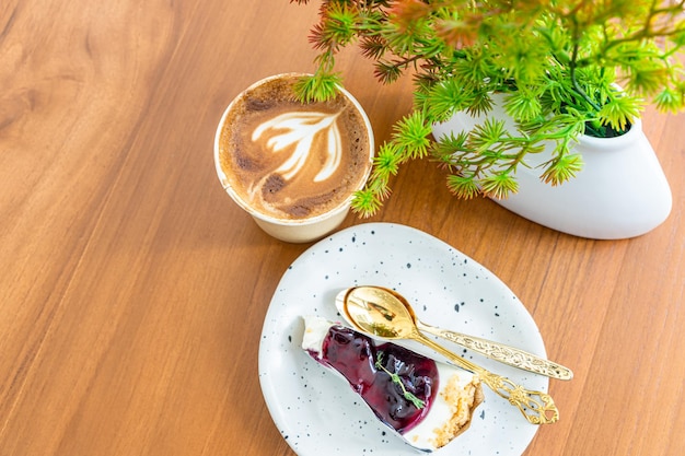 Heißer Kaffee Latte mit Latte Art Milchschaum in einer Tasse aus Papier und Blaubeerkuchen auf Holzschreibtisch in der Draufsicht Als Frühstück in einem Café im Cafeduring Business Work Concept