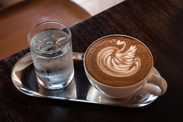 Heißer Kaffee Latte mit Latte Art Milchschaum in Schwanenform in Tassenbecher auf Holzschreibtisch in der Draufsicht Als Frühstück in einem Café im Cafeduring Business Work Concept