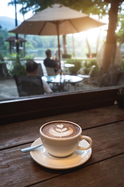 Heißer Kaffee Latte mit Latte Art Milchschaum in Tasse Becher auf Holzschreibtisch in der Draufsicht Als Frühstück in einem Café im Café während des Geschäftsarbeitskonzepts