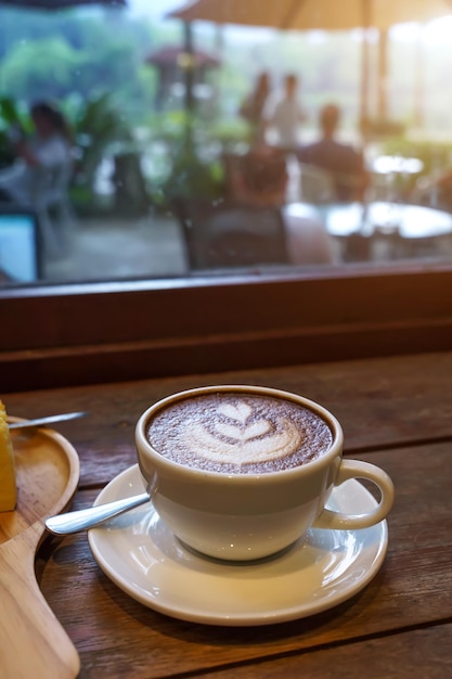 Heißer Kaffee Latte mit Latte Art Milchschaum in Tasse Becher auf Holzschreibtisch in der Draufsicht Als Frühstück in einem Café im Cafeduring Business Work Concept