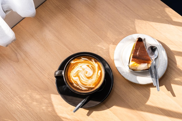 Heißer Kaffee Latte mit Latte Art Milchschaum in Tassenbecher und hausgemachter Schokoladenkuchen Holzschreibtisch auf Holzschreibtisch in der Draufsicht Als Frühstück in einem Café im Café während des Geschäftsarbeitskonzepts