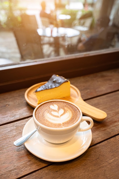 Heißer Kaffee Latte mit Latte Art Milchschaum in Tassenbecher und hausgemachter Schokoladenkuchen Holzschreibtisch auf Holzschreibtisch in der Draufsicht Als Frühstück in einem Café im Café während des Geschäftsarbeitskonzepts