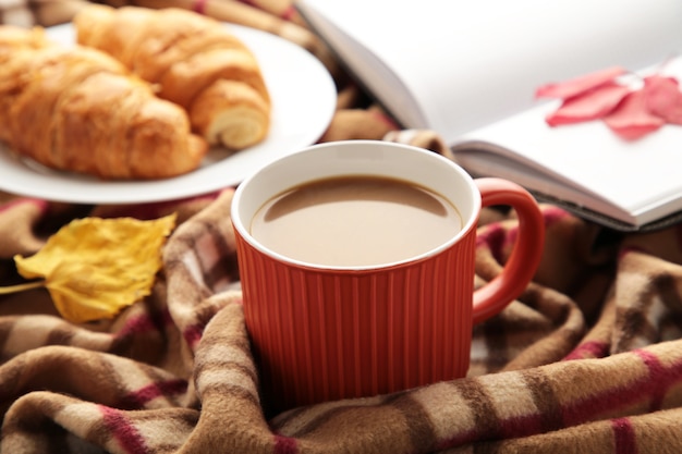 Heißer Kaffee mit Croissant und Herbstlaub auf Plaid - saisonales Entspannungskonzept