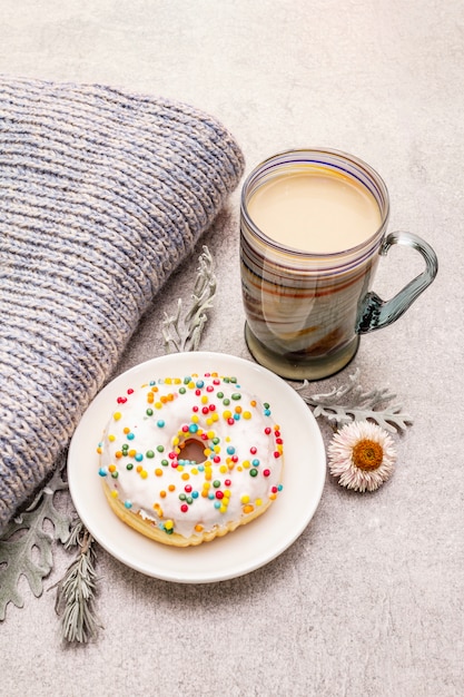 Heißer Kaffee mit einem Donut. Wintergetränk für gute Laune mit Pullover, Blättern und Blüten.