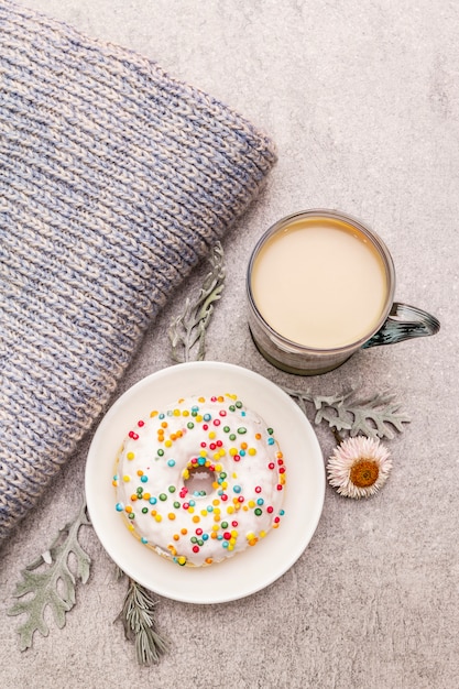 Heißer Kaffee mit einem Donut. Wintergetränk für gute Laune mit Pullover, Blättern und Blüten.