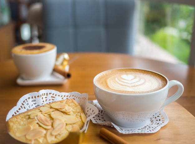 Heißer Kaffee mit Latte Art in einer weißen Tasse mit Mandelbrot auf dem Holztisch.