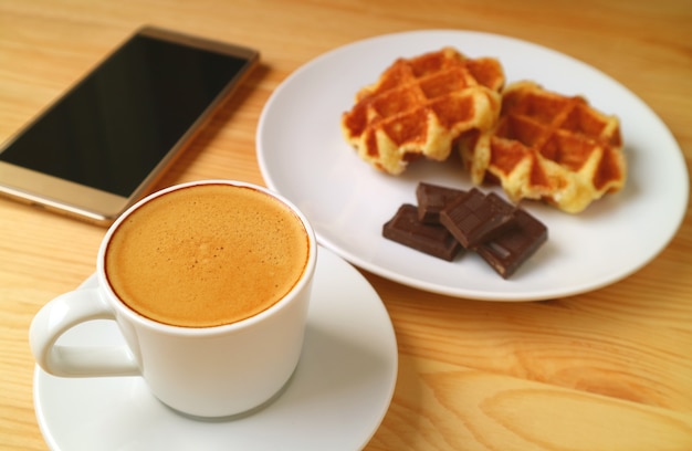 Heißer Kaffee mit verschwommenen Süßigkeiten und Handy mit leerem Bildschirm